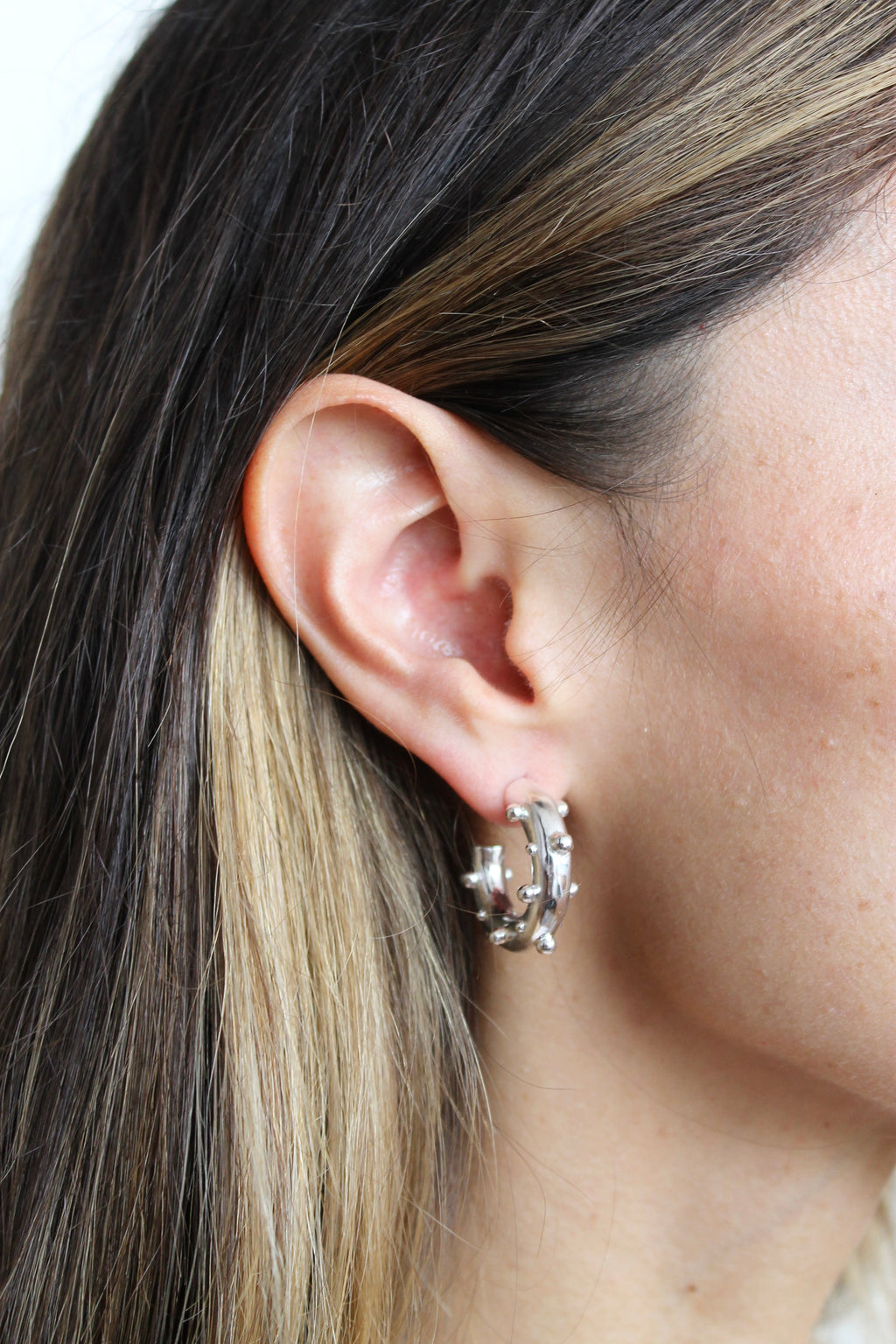 Close-up of an ear wearing a silver earring with a blurred background