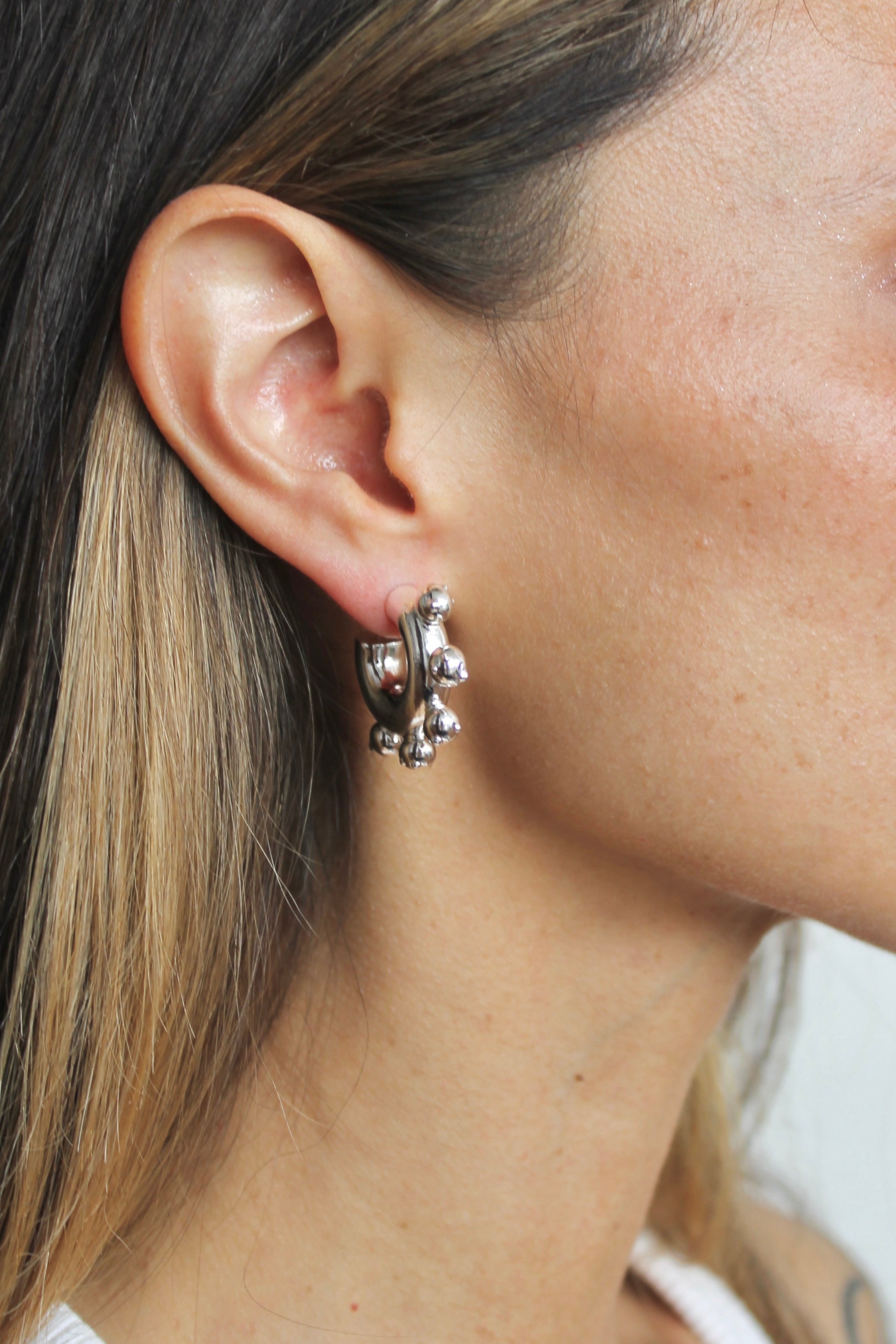 Close-up of an ear wearing a silver earring with a blurred background