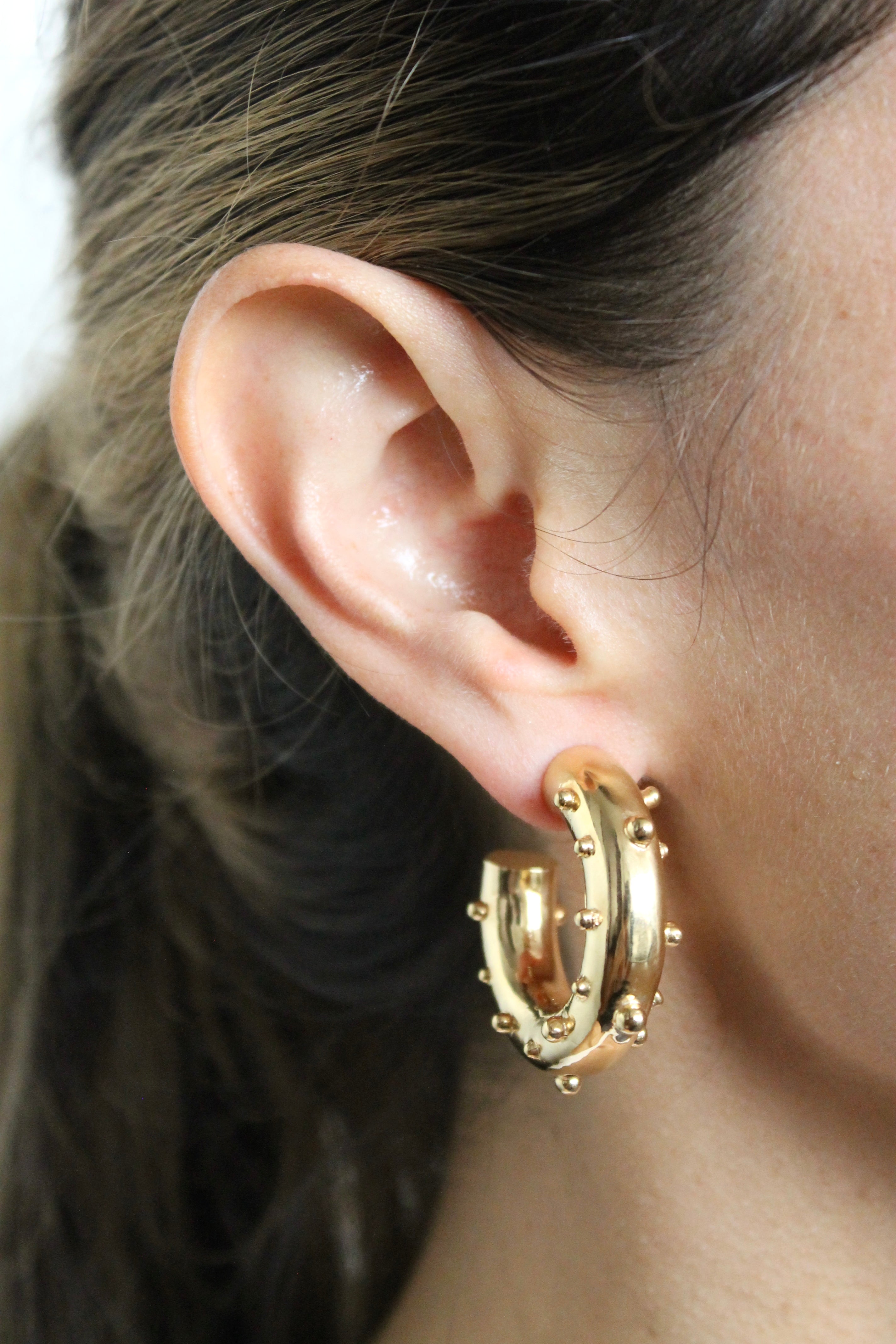 Gold hoop earring worn by a person with dark hair.