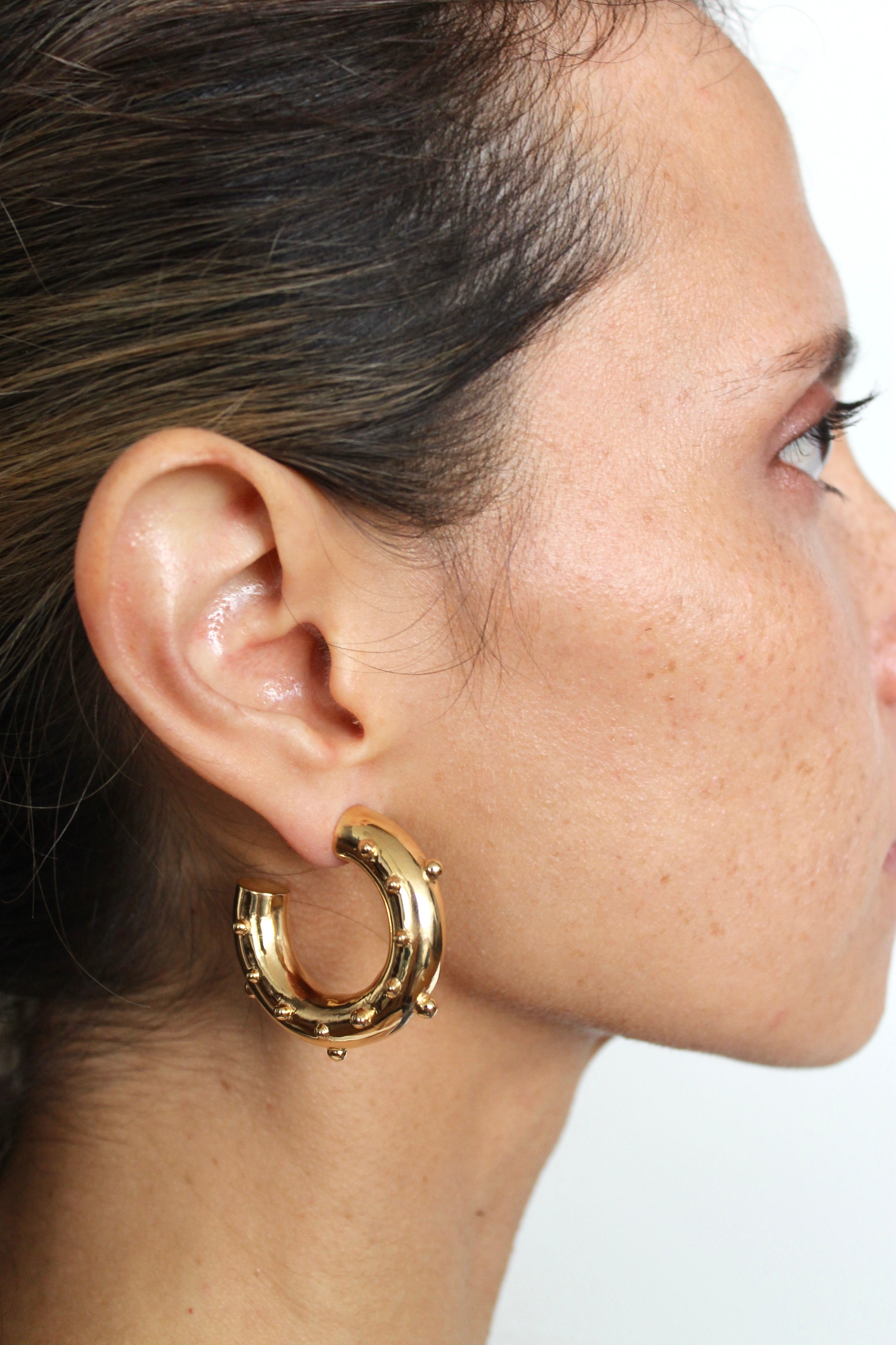 Gold hoop earring worn by a person on a white background