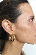 Close-up of a person wearing gold hoop earrings with a neutral background